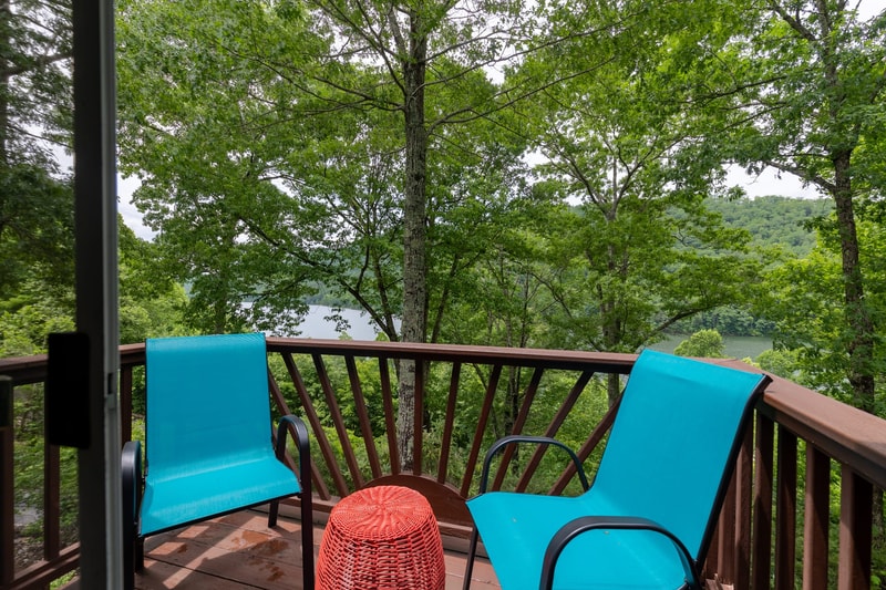 Two turquoise chairs on the upper balcony with lake water visible through summer foliage.