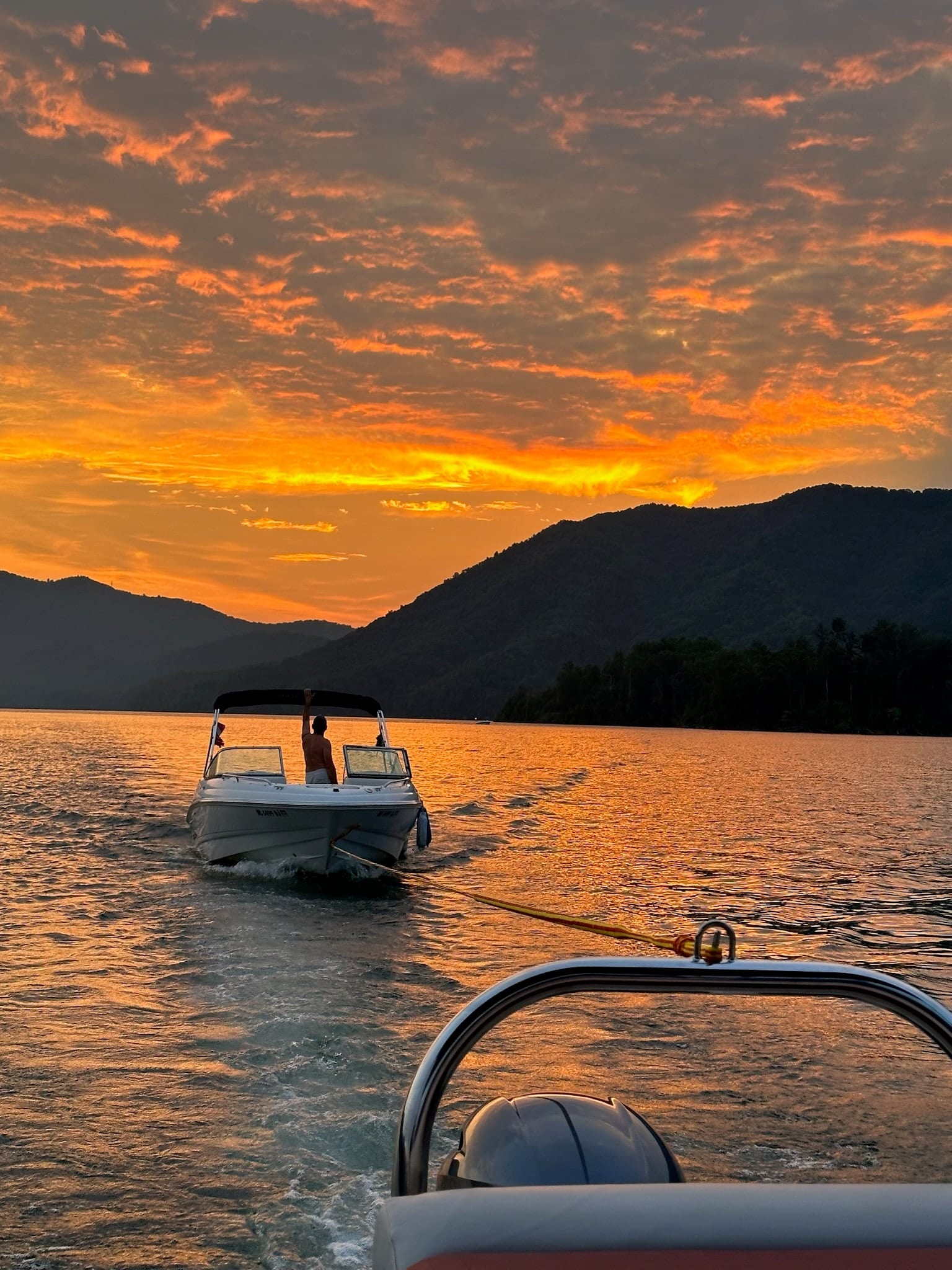 Boat towing a tube across Watauga Lake under a fiery orange sunset sky.