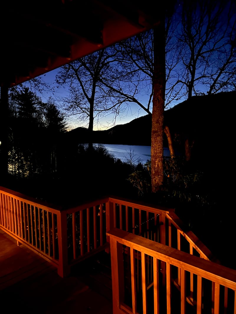 Lake house deck at blue hour with Watauga Lake visible through bare trees.