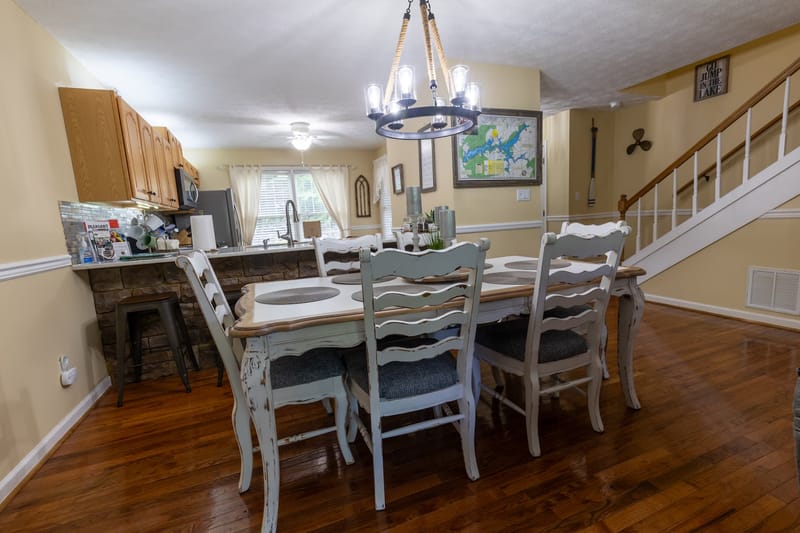 Dining area set for six with farmhouse table and chandelier, open to the kitchen.