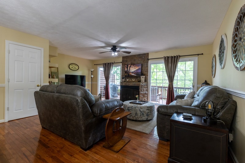 Living room with stone fireplace, ceiling fan, and doors out to the deck.