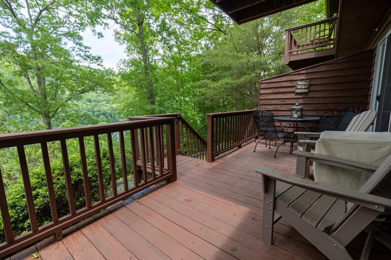 Wooden upper deck with seating, surrounded by hardwood trees in full summer.