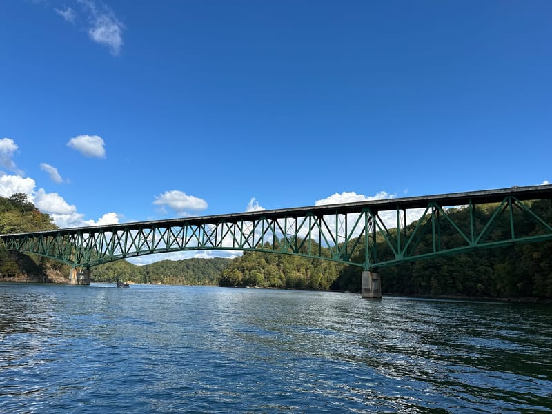 Steel truss bridge spanning Watauga Lake under a bright blue summer sky.