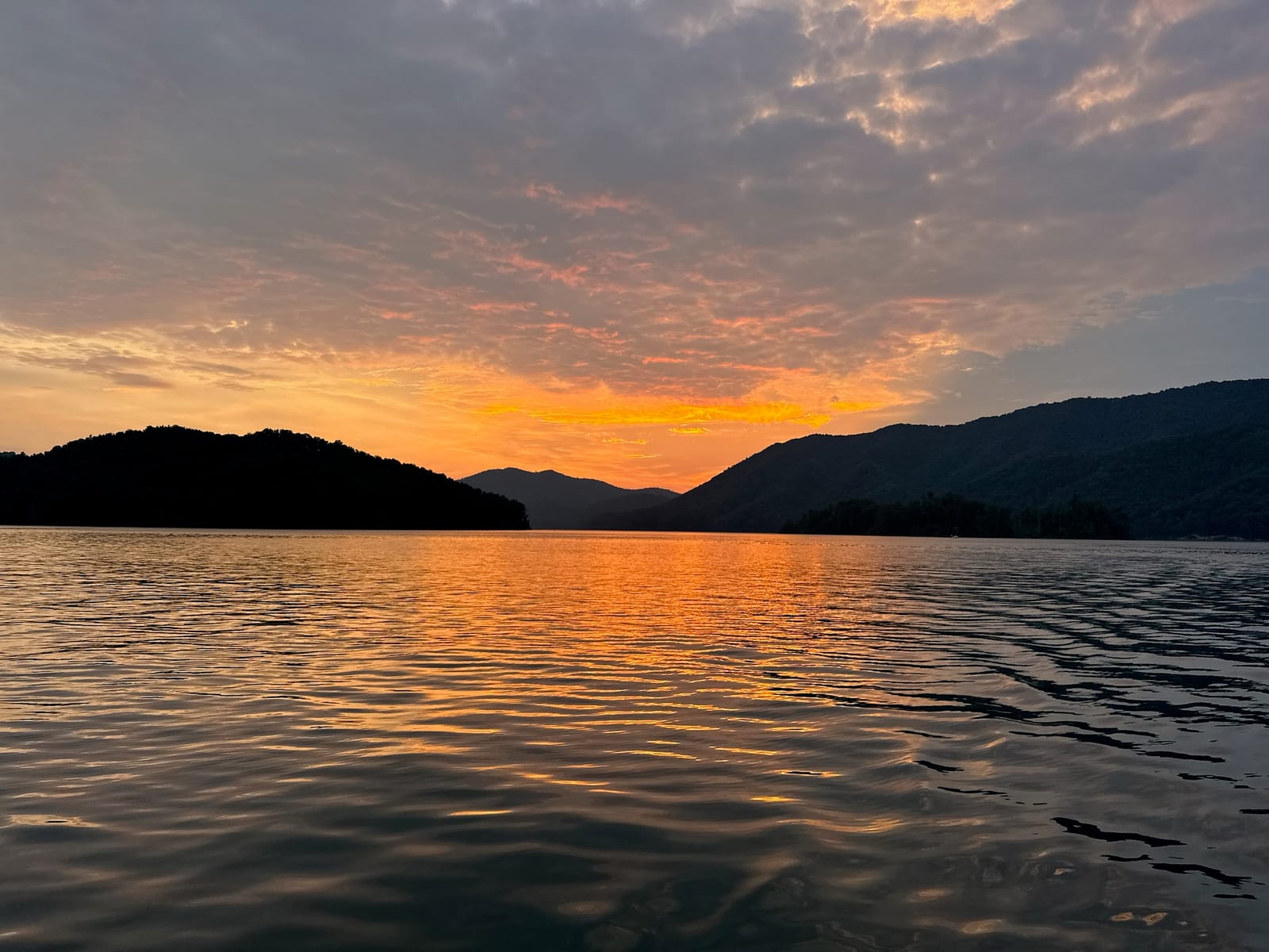 Wide sunset over Watauga Lake with mountain silhouettes and glowing water.