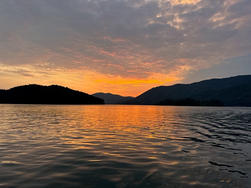 Wide sunset over Watauga Lake with mountain silhouettes and glowing water.