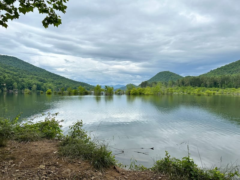 Watauga Lake reflecting twin green peaks under a soft cloudy summer sky.
