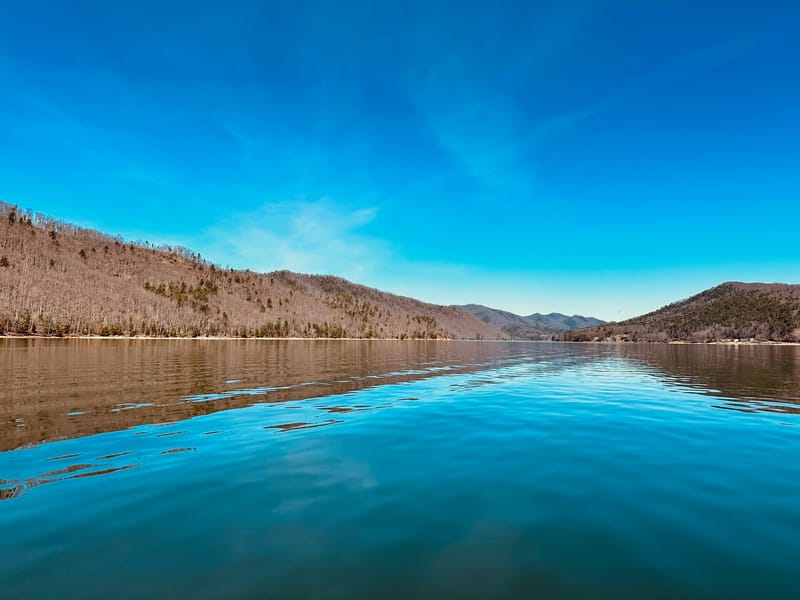 Crystal blue Watauga Lake and bare winter mountains under a deep blue sky.